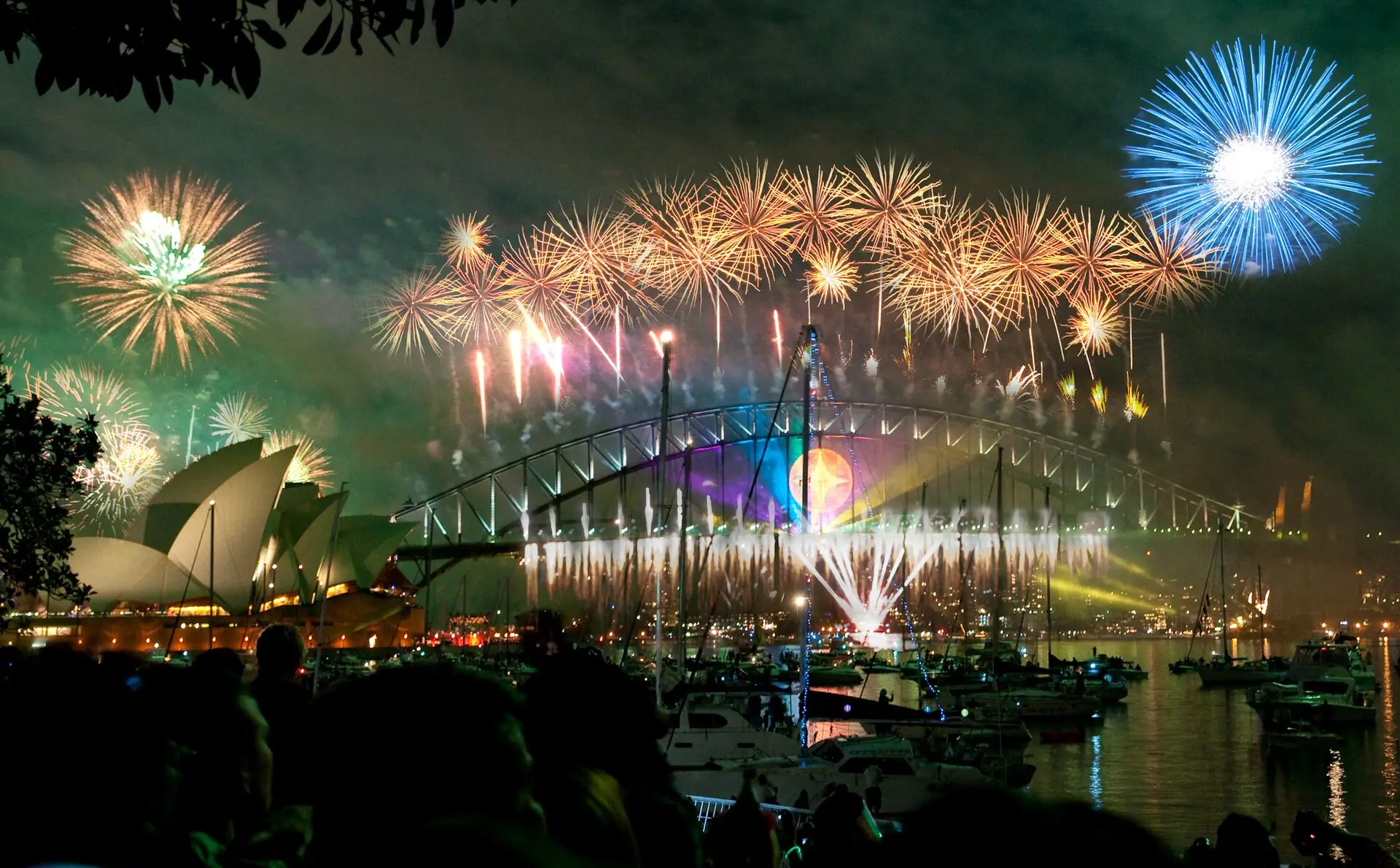 A crowd watching gold fireworks over the Sydney Harbour Bridge and Opera House